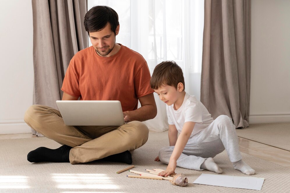 A parent and child sit on a soft carpet, engaged with a laptop, surrounded by art supplies and papers in a cozy living room.