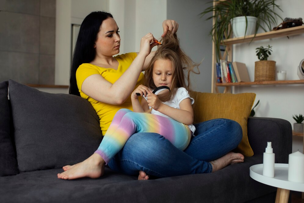 A woman styles a child's hair while seated on a couch, surrounded by a cozy, modern living space with plants and books.