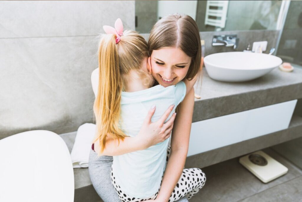 A mother and daughter share a tender embrace in a modern bathroom, surrounded by neutral tones and stylish fixtures.