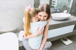 A mother and daughter share a tender embrace in a modern bathroom, surrounded by neutral tones and stylish fixtures.