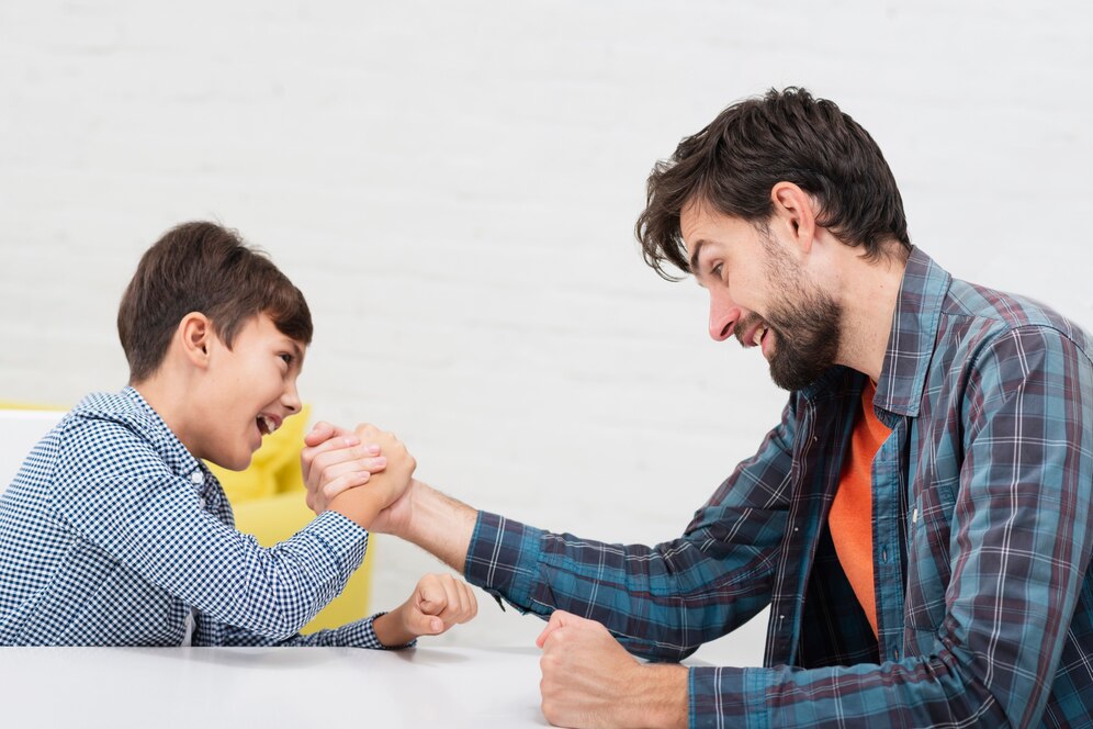 A child and an adult engaged in an arm wrestling match at a table, showcasing friendly competition and playful determination.