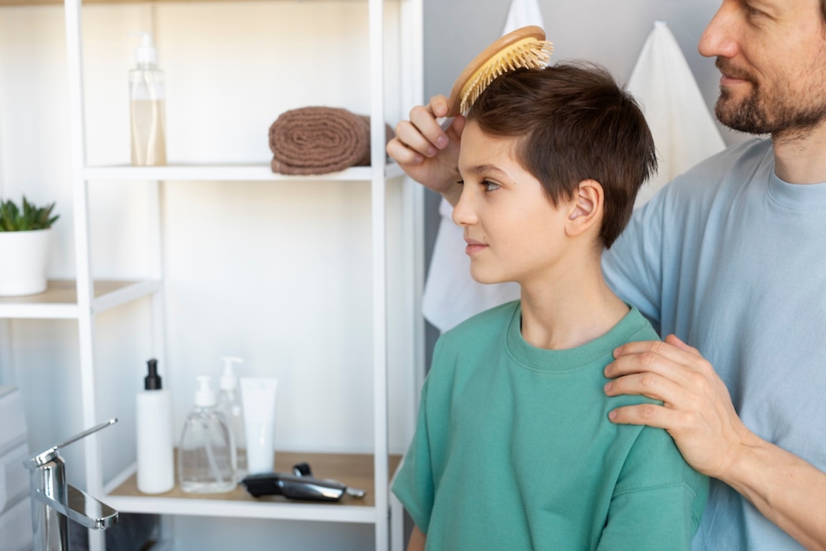 A person brushes the hair of a child in a modern bathroom, surrounded by towels, skincare products, and a small plant.