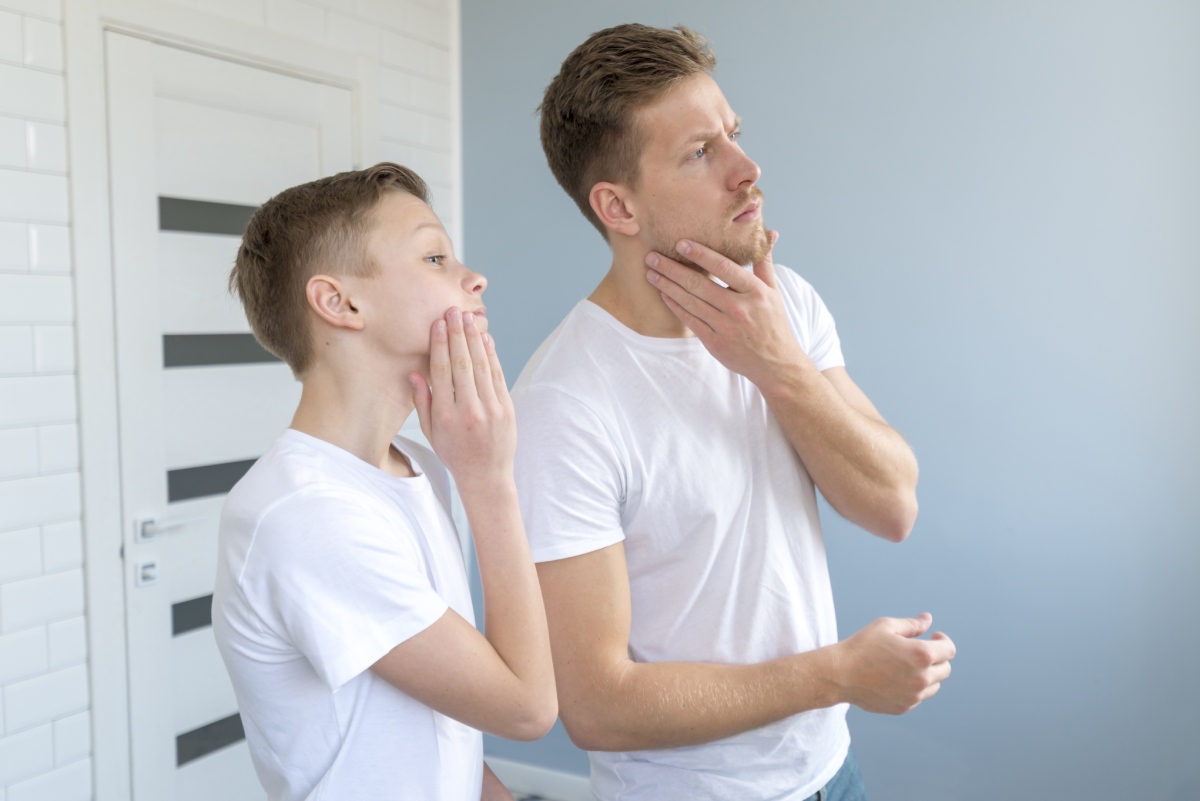 Two individuals in white t-shirts stand in a modern room, contemplating thoughtfully with their hands on their chins.