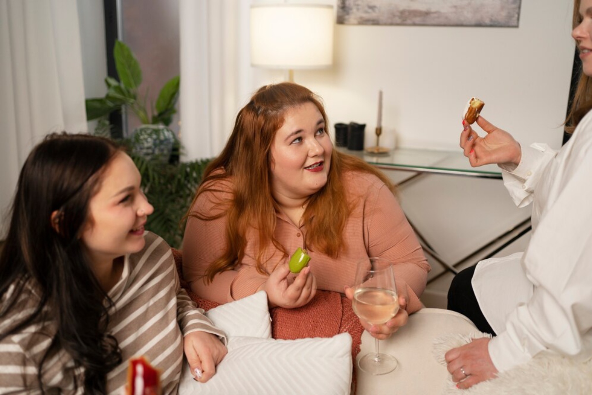 Three friends share a cozy gathering, enjoying snacks and drinks, with a modern interior and soft lighting creating a warm atmosphere.