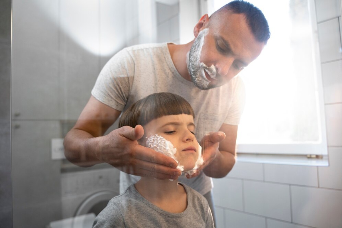 A person gently holds a child’s face in a well-lit bathroom, preparing for a grooming activity, with a washing machine in the background.